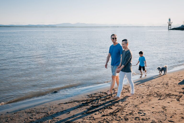 Two dads and a child walking their dog on a scenic beach, enjoying quality time.
